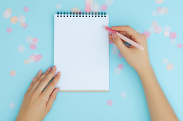 Well-groomed female hands with a pen near a notebook on a blue background. To-do list. Notes. Blank sheet for text.