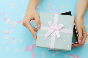 Well-groomed female hands hold a gift on a blue background. Festive background. Surprise.