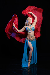 Young woman belly dancer in a blue oriental costume on a black background