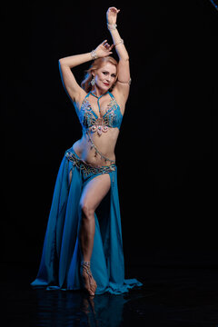 Young woman belly dancer in a blue oriental costume on a black background