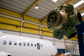 A white airplane is in a hangar with a green and black machine. The machine is a propeller and is attached to the airplane