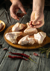 Hands are seen seasoning fresh chicken thighs with spices and herbs on a wooden cutting board, surrounded by dried chili peppers and garlic cloves in a cozy kitchen atmosphere