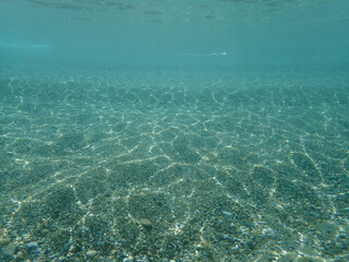 Dark blue ocean surface seen from underwater. Abstract waves underwater and rays of sunlight shining through, Sun light rays undersea deep, Underwater background with sea bottom, Mediterranean sea.