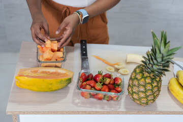 Woman preparing tropical fruit salad with papaya, pineapple, strawberries and bananas