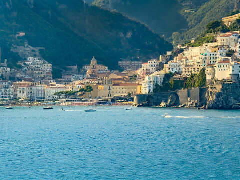 Amalfi, Salerno, Italy - July 6, 2024: The town seen from Tyrrhenian Sea, lies at the mouth of a deep ravine, at the foot of Monte Cerreto. Cathedral tower and Mandingo beach. All under evening sun