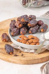 Medjool dates and almonds on a plate with a spoonful of shredded coconut, set on a wooden board with a jar of dates in the background