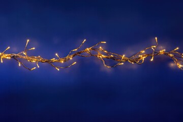 Warm golden Christmas garland lights softly glowing, creating a dreamy bokeh effect over a deep blue background