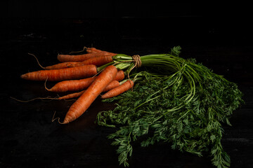 View of a bunch of carrots with green leaves on a dark table, horizontal with copy space