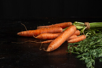 Top view of a bunch of carrots with green leaves on a dark table, horizontal with copy space