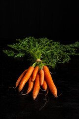 Aerial view of a bunch of carrots with green leaves on a dark table, vertical with copy space