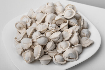 A plate full of raw, frozen pelmeni, traditional dumplings made of dough filled with meat, showcasing their distinct shape and texture.