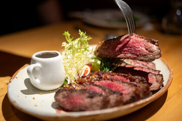 A fork on medium rare wagyu meat served on plate with sauce and vegetable