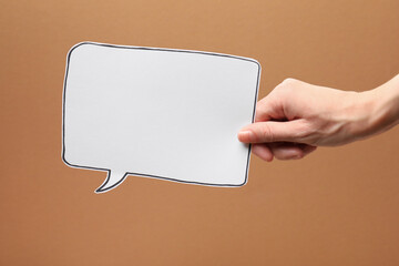 Woman holding blank speech bubble on brown background, closeup. Space for text