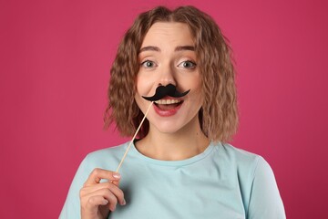 Happy woman with fake paper mustache on pink background