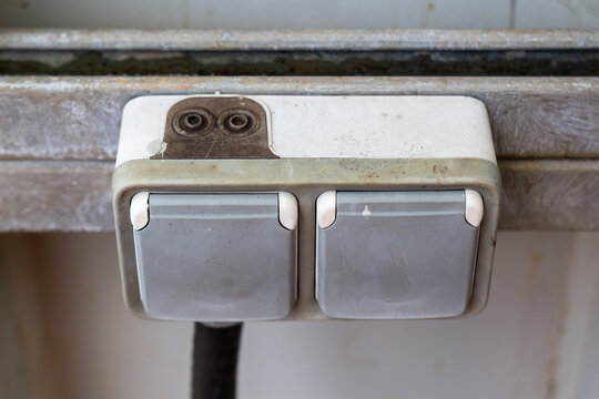 Close up of a weathered dual electrical outlet mounted on a worn metal surface