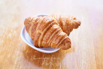 Golden croissants on white plate - freshly baked pastries on wooden table.