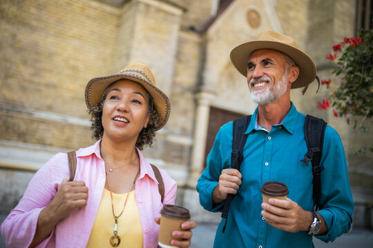 Elderly married couple drinking coffee to go in the city center. Tourists exploring the city.
