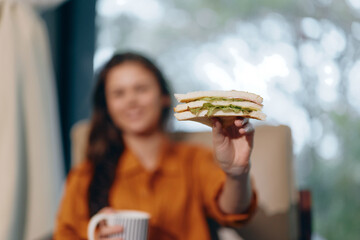 A woman holding a delicious sandwich with lettuce, sitting in a cozy chair, enjoying healthy eating...
