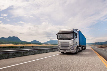 Obraz premium A large semi truck is driving down a road with mountains in the background