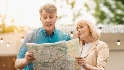 Mature husband with his wife reading map near camper van in countryside