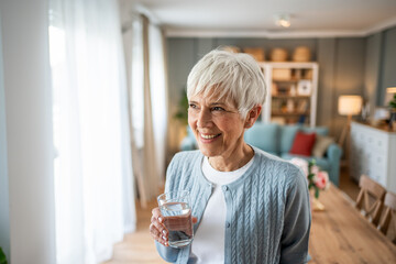 Senior woman drinking water and looking out the window in her kitchen