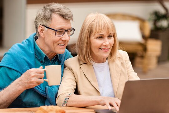Affectionale elderly couple watching movie on laptop during vacation in countryside