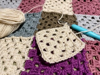 Crochet granny square, clews and hook on crochet blanket background photo	