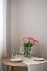 A beautiful bouquet of pink tulips beside a glasses for wine, candles, plates enhance home decor and ambiance. Table serving.