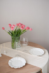 A beautiful bouquet of pink tulips beside a glasses for wine, candles, plates enhance home decor and ambiance. Table serving.