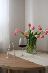 A beautiful bouquet of pink tulips beside a glass of rich red wine, candles enhance home decor and ambiance.