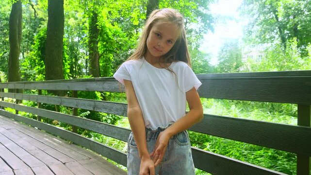 Close up portrait little child in green forest slow motion. Happy kid girl walk on wooden bridge in nature park on summer vacation