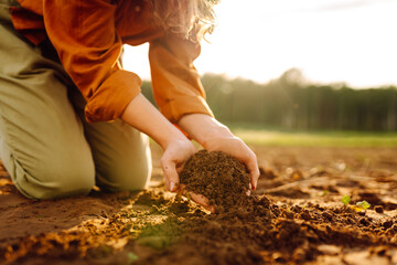 Close-up of farmer's hands holding fertile soil. Young female agronomist checking soil quality...