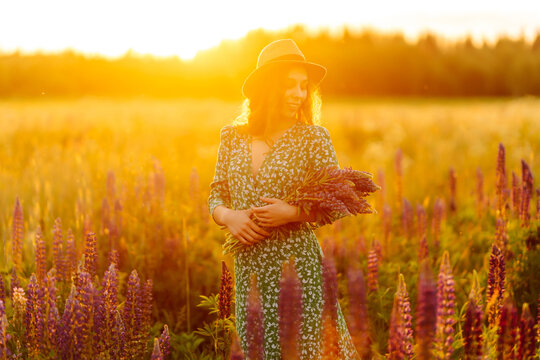 Smiling woman having fun at sunset in purple flowers field. Beautiful woman with wildflower bouquet enjoying nature. Relaxation, posing concept.