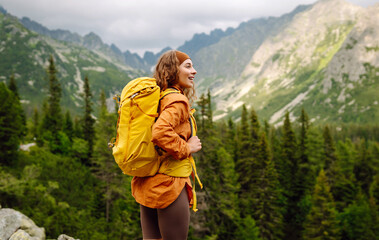 An active female traveler with a bright hiking backpack enjoys the mountain view from the cliff....