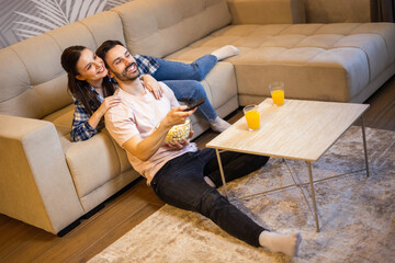 Couple laying on the couch of their living room and watches movies. They eat popcorn and drink...