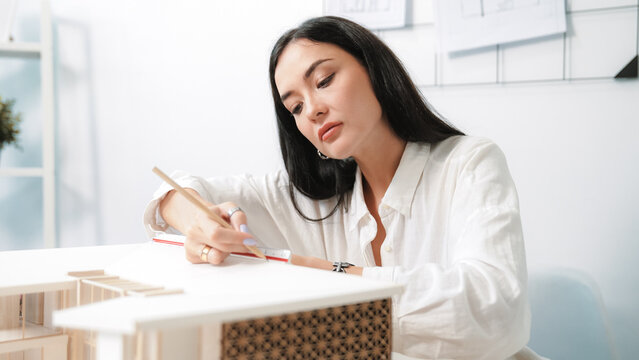 Closeup portrait image of professional young beautiful engineer architect using triangular scale measures house model with focusing at modern office. Business creative design concept. Immaculate.