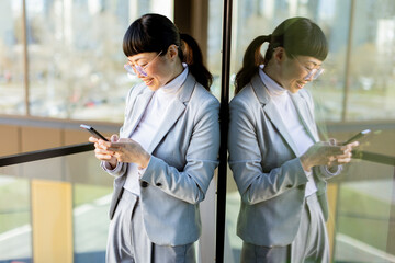 Professional Asian woman engaged in text messaging while taking a break in a modern office setting