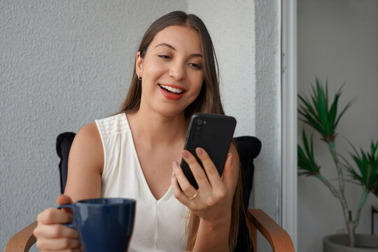Brazilian business woman using smartphone for videocall on her apartment balcony in the morning