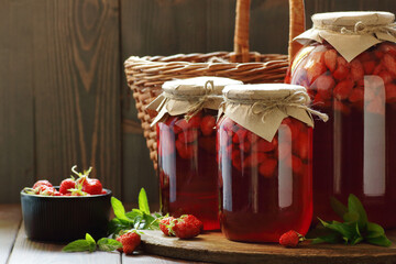 Jars with strawberry compote with fresh berry and mint leaves on wood and rustic background, cottagecore aesthetic, copy space, batch cooking, sustainable living, zero waste storage concept