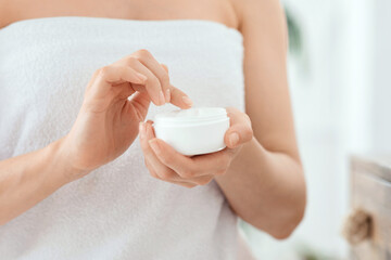 Closeup of woman wrapped in towel holding jar with cream, home interior, free space