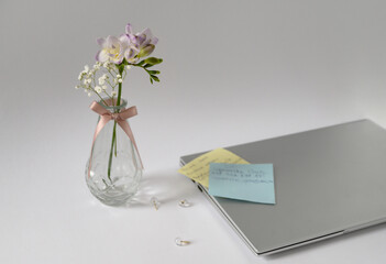 A stylish office setup featuring a laptop, a glass vase with fresh flowers, and handwritten notes on a clean white surface. Perfect for productivity, planning, and creative work.
