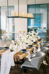 Black plates stand near white bouquets of flowers on a festive table in a restaurant with candles on a hanging shelf