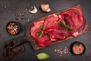 Raw organic steak with ingredients for cooking on a dark slate, stone or concrete background. Top view with copy space. High quality photo