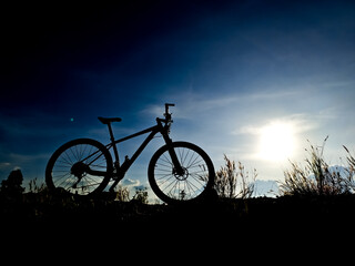 Obraz premium Silhouette of Mountain Bike Against Dramatic Sunset Sky in Outdoor Adventure Landscape Setting