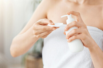 Cropped of woman wrapped in towel using face lotion and cotton pad, home interior, copy space