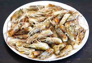 Fresh shrimps on white round plate isolated in selective focus. Shrimp head