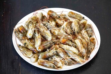 Fresh shrimps on white round plate isolated in selective focus. Shrimp head