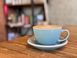 Gorgeous and Beautiful Latte Art Served in a Charming Blue Cup on a Cozy Wooden Table. A warm and cozy latte featuring intricate and beautiful art presented in a vibrant blue cup on a wooden surface