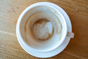 An empty white cup of drunken cappuccino with foam around the edges of the cup stands on a white...