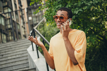 Obraz premium Young man enjoying a phone conversation while taking a stroll in the city on a sunny day with trendy sunglasses and a casual outfit